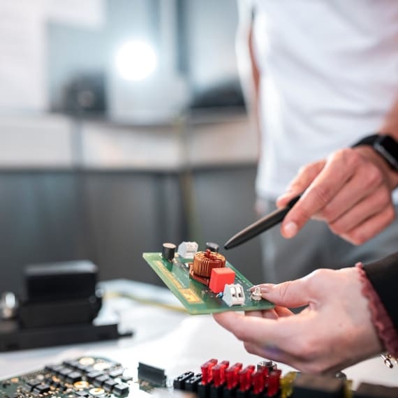 A man is pointing on electronic components on a circuit board with a pen