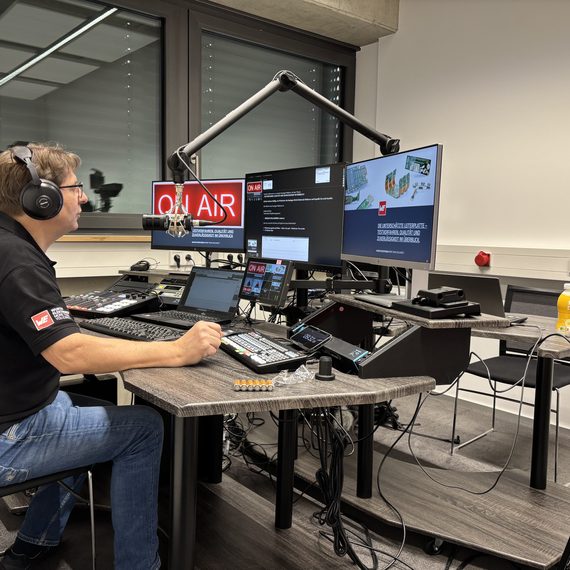 Der Moderator des Webinars sitzt im Medienraum vor den Bildschirmen und moderiert