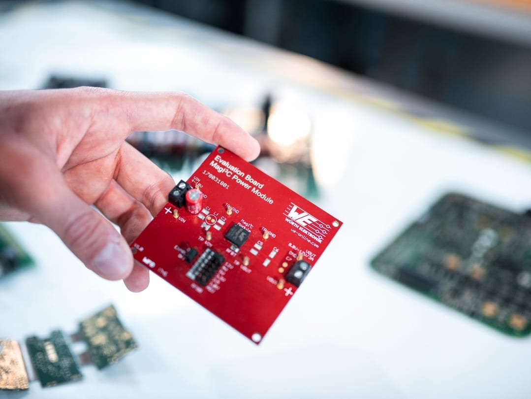 Eine Hand hält eine rote Leiterplatte mit elektronischen Bauteilen