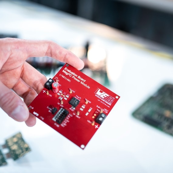 Eine Hand hält eine rote Leiterplatte mit elektronischen Bauteilen