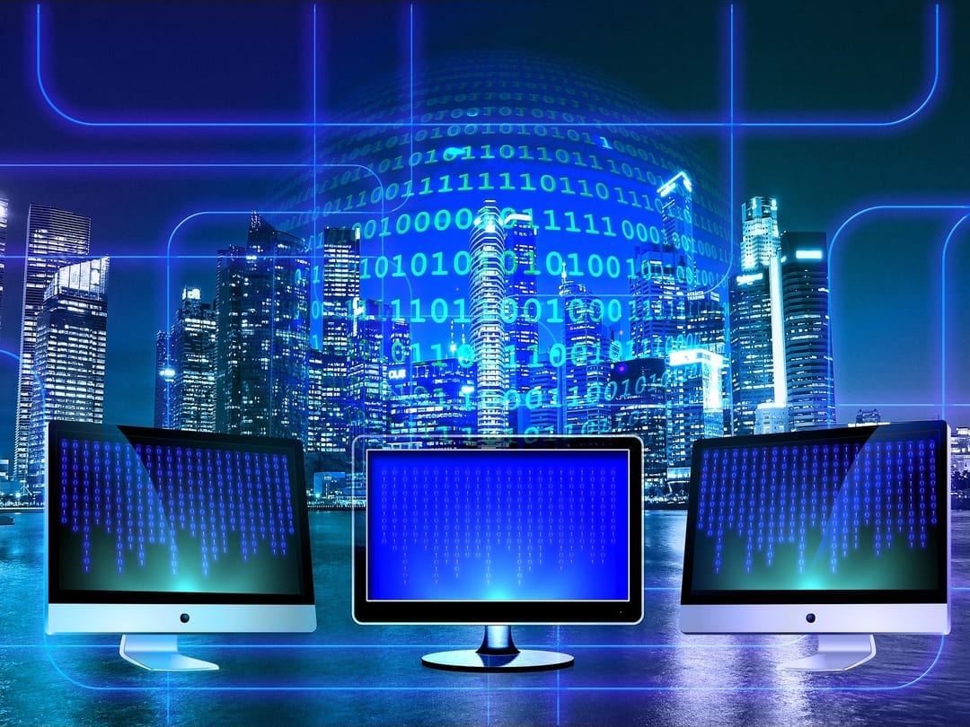 Three computer monitors with a cityscape and coding in the background