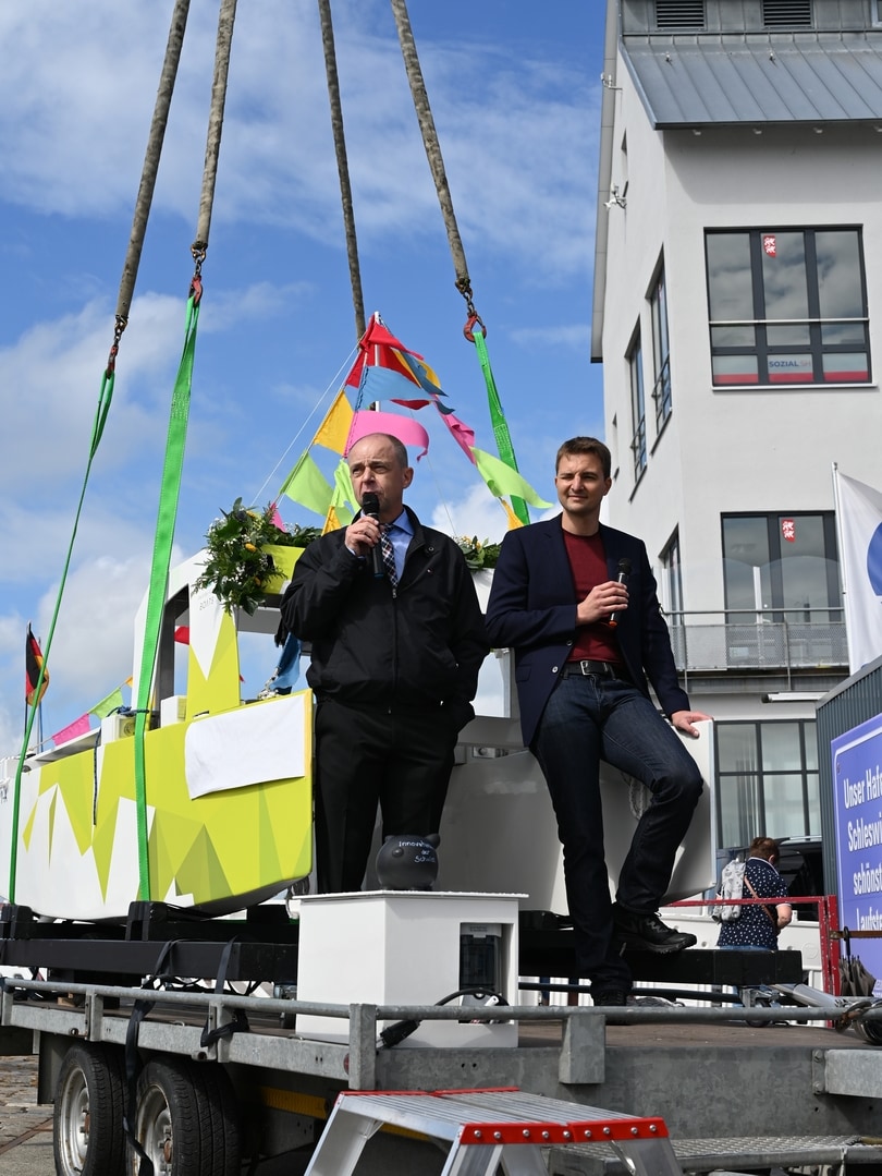 Zwei Männer stehen bei schönem Wetter auf einem Schiff und halten eine Rede