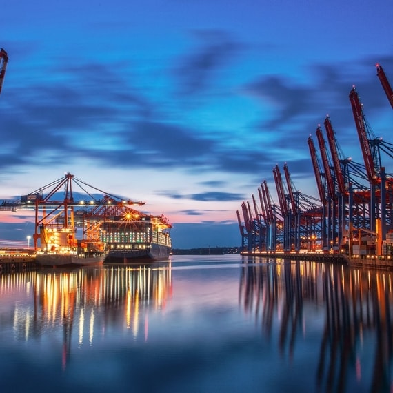 Bild zeigt ein Frachtschiff an einem abendlichen Containerterminal