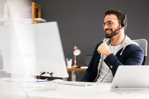 Male person with a headset sits in front of a computer screen