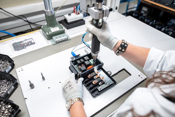 Produktionsmitarbeiter, welcher eine Leiterplatte in einer Box verschraubt.