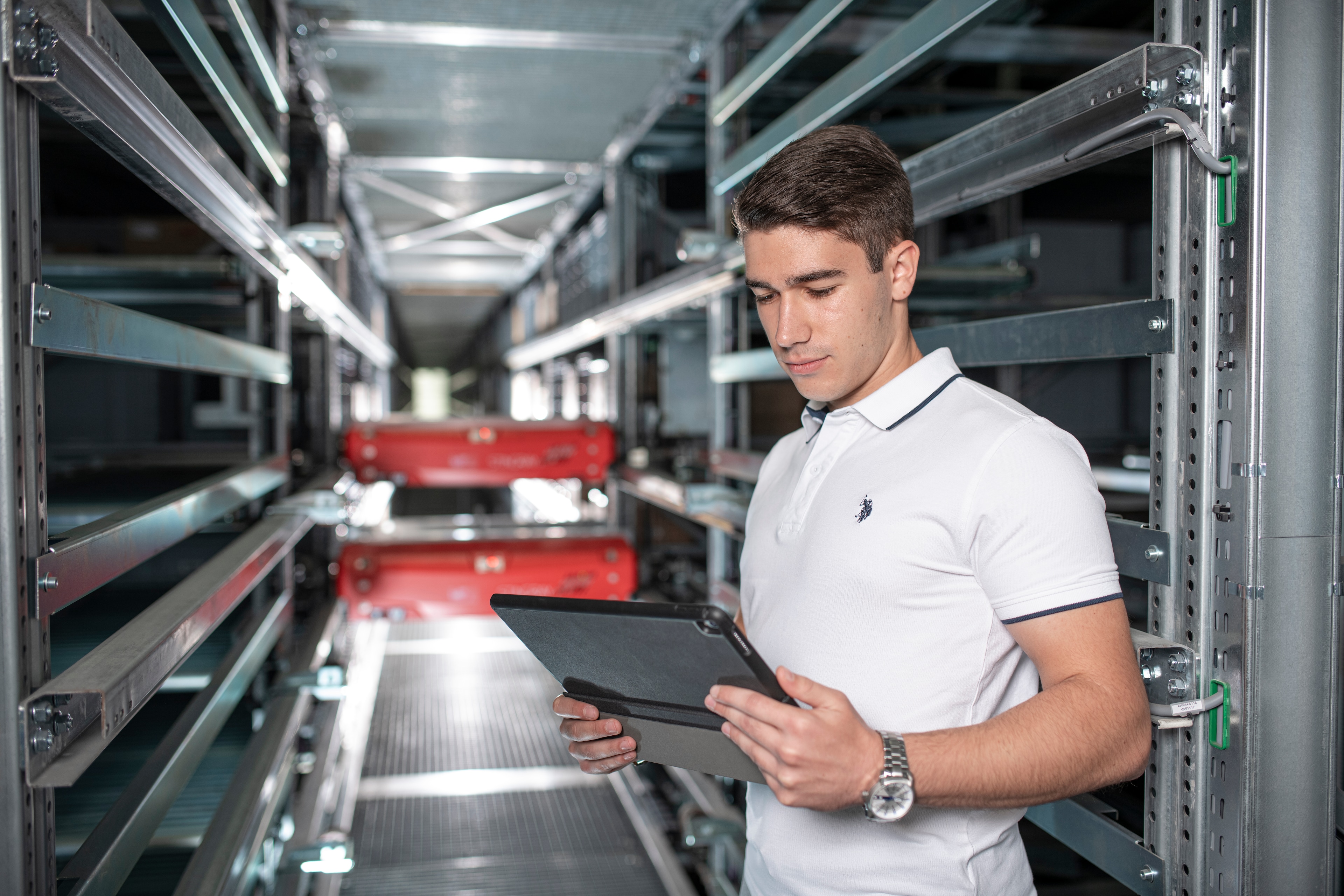 Praxiserfahrung Ein Mann steht zwischen Regalen in der Logistik und hält ein Tablet in der Hand