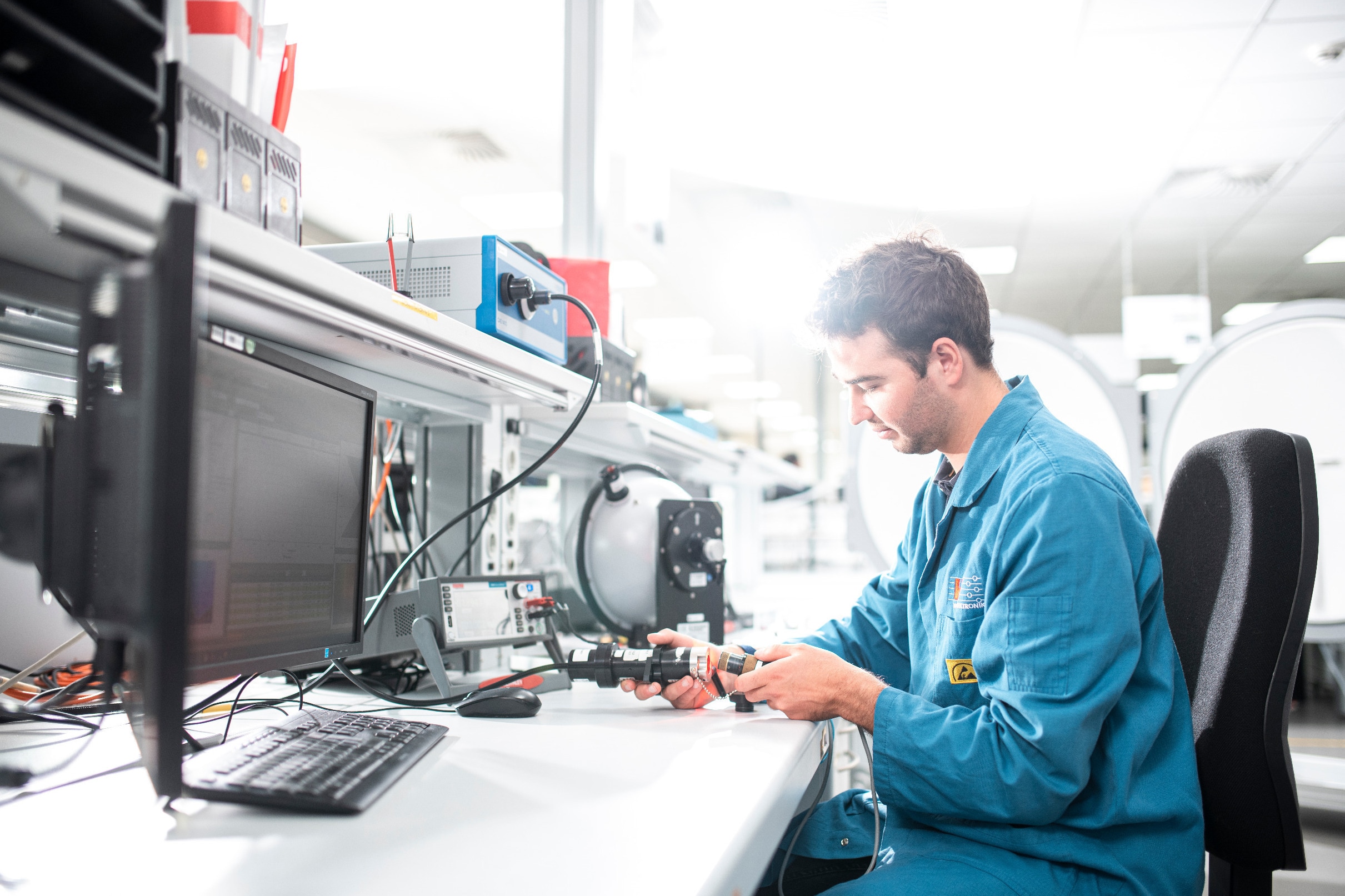 Health and safety - work in the laboratory A person in occupational safety clothing sits at a desk in the laboratory with an experimental setup in front of them