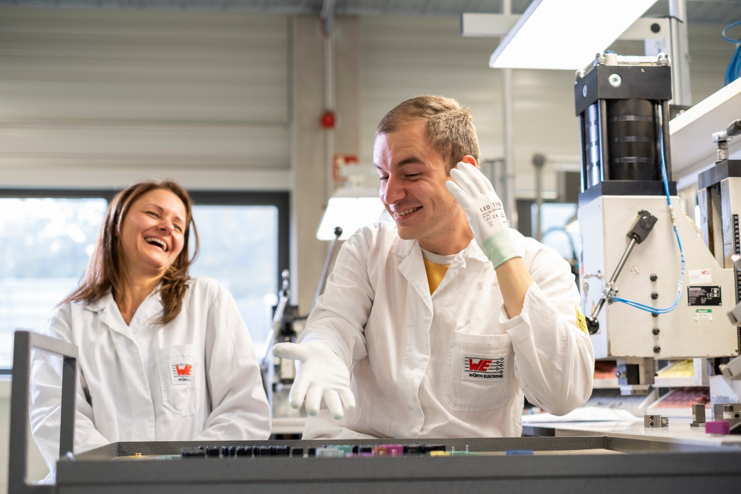 Discussion in Laboratory Two person are sitting in front of a circuit board and laughing