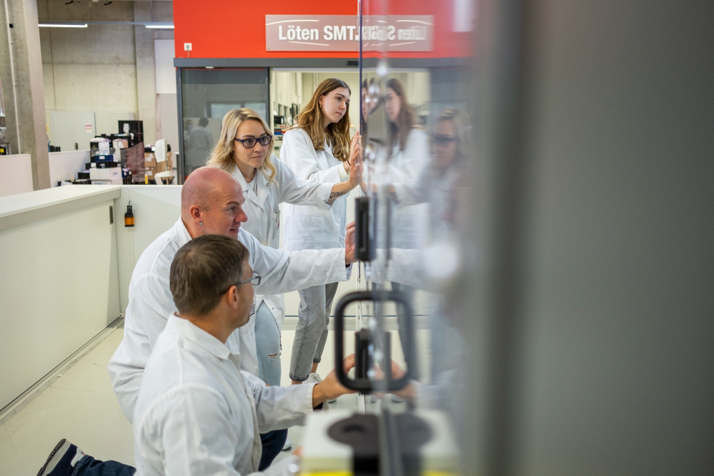 internship students Two women and two men are standing in front of a cupboard looking inside, the two men are kneeling on the floor, all four people are wearing lab coats. They are also in a laboratory