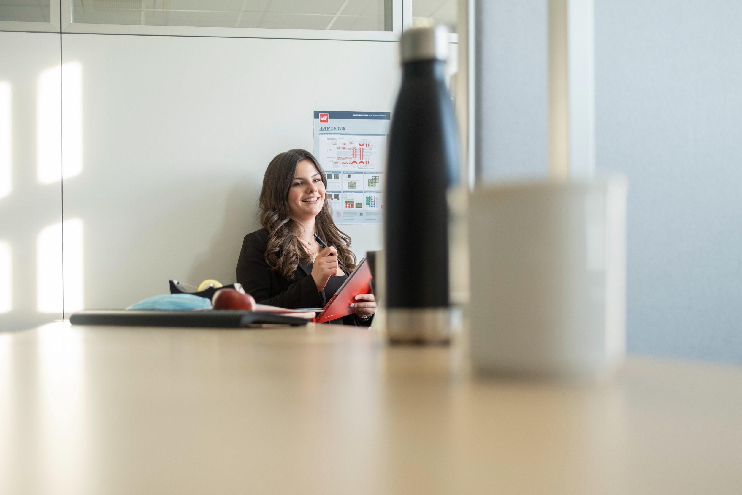 internship A woman is standing at a counter and looks thoughtful. She is holding a red write board and you can also see a bottle and a cup in the foreground.