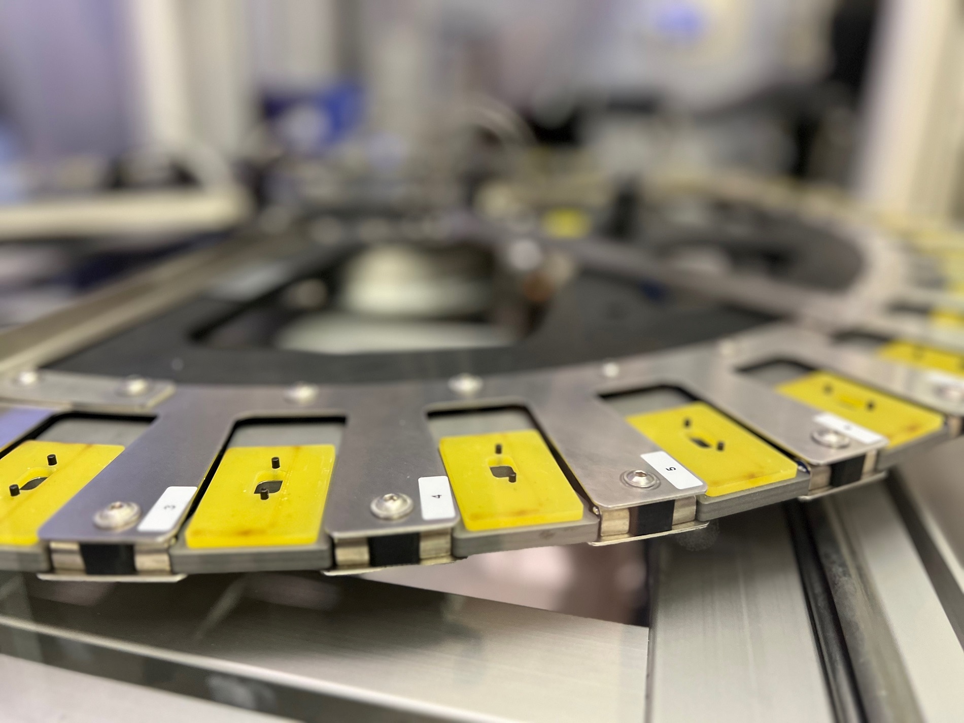 Nahaufnahme eines runden industriellen Maschinenteils mit gelben und schwarzen Segmenten, Metallrahmen und verschiedenen Markierungen. Der Hintergrund ist unscharf.