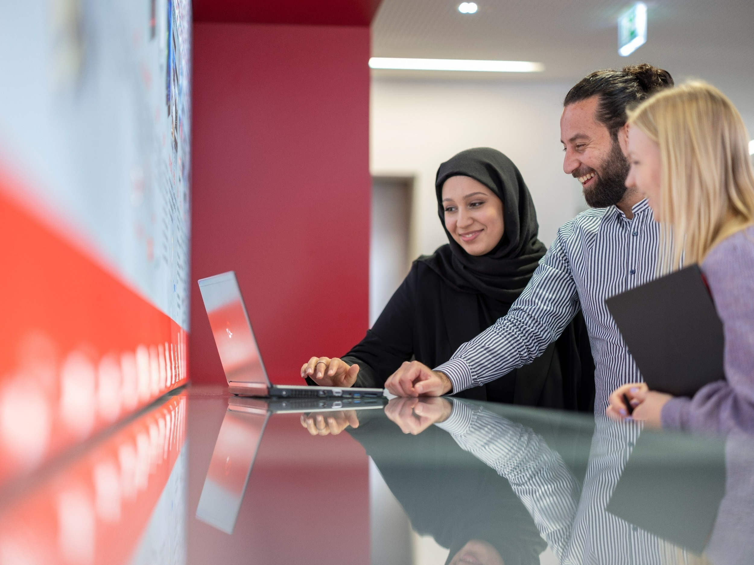 working students Two women and a man look in front of a laptop and smile, one woman holds another laptop under her arm